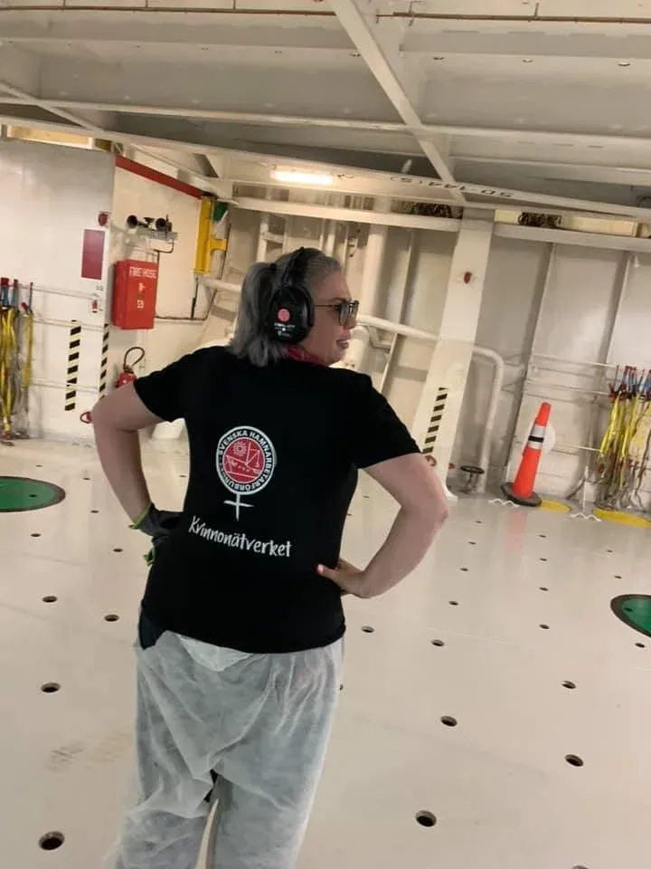 En hamnarbetare i svart t-shirt med Kvinnonätverkets emblem på ryggen, ombord på ett fartyg